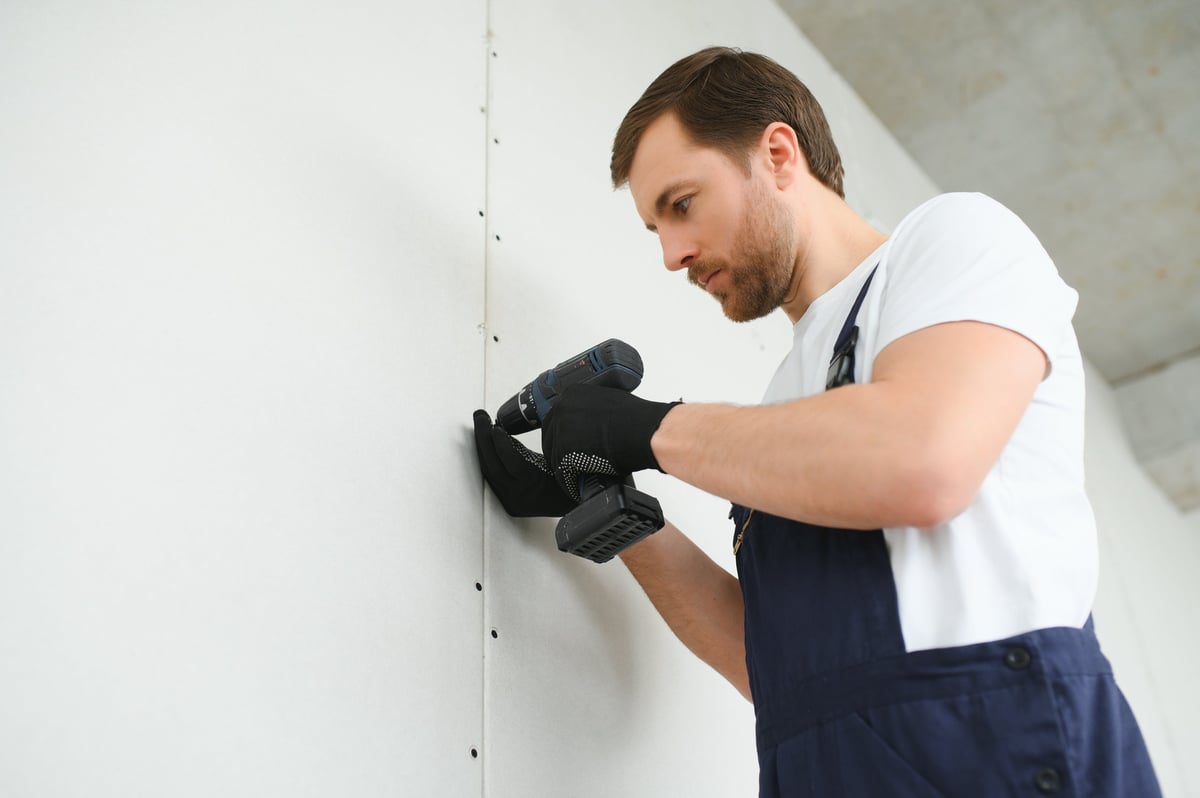 Worker builder installs plasterboard drywall at a construction