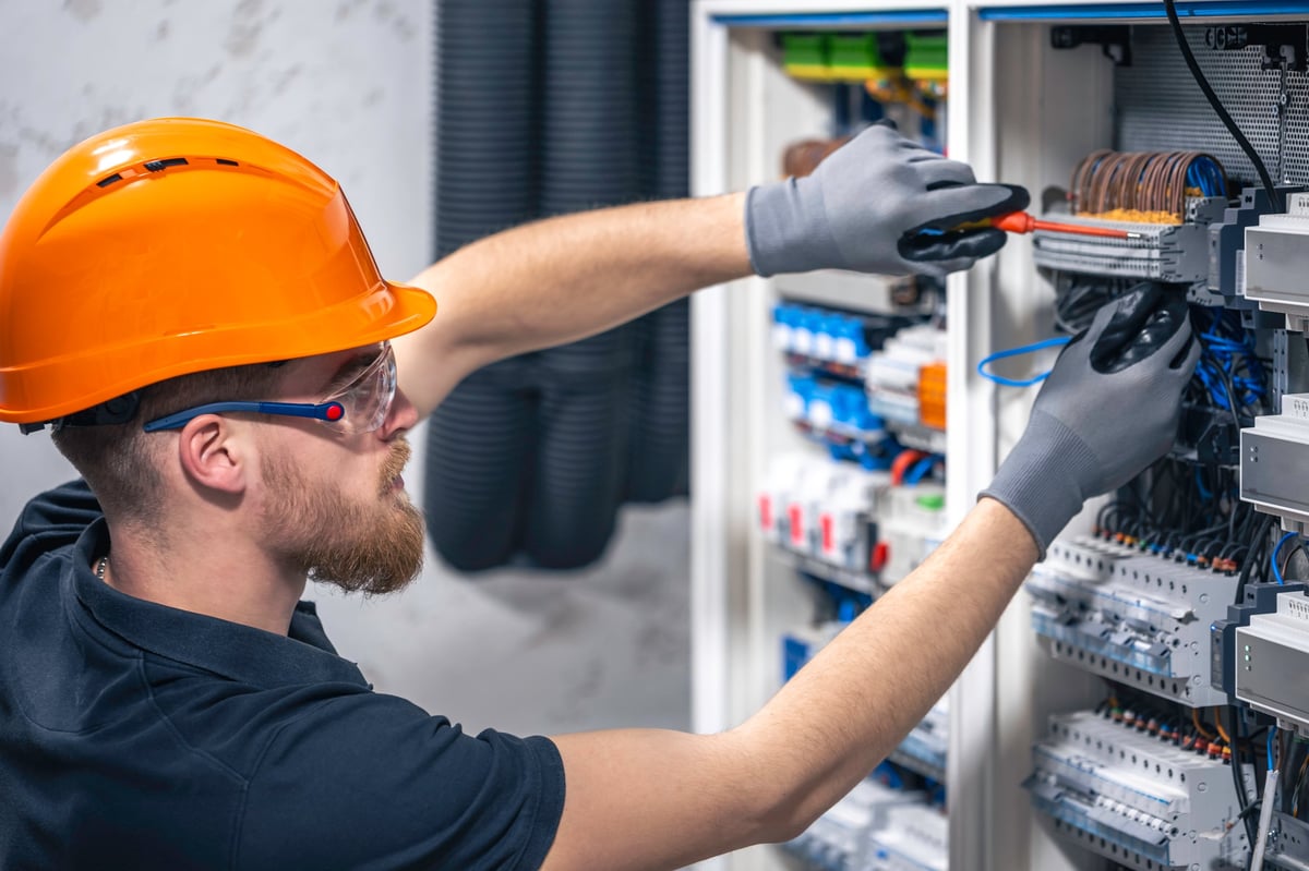 A male electrician works in a switchboard with an electrical connecting cable.