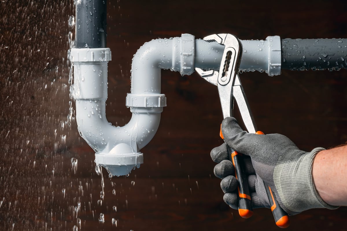 Close up of a plumber hand fixing a water leak in a sink drain siphon pipe with an adjustable pliers.