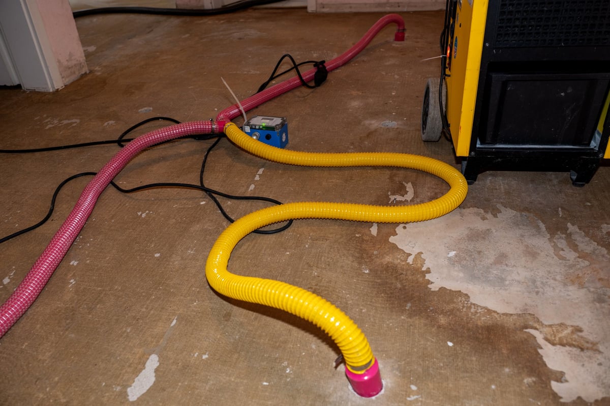 Water damage restoration using a professional industrial building drying unit with dehumidifiers and pipes to remove water and moisture from the wet floor and screed